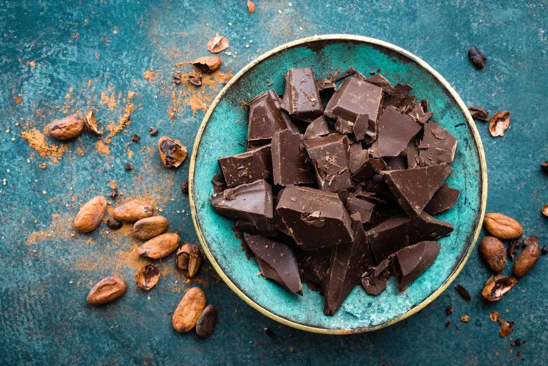 pieces-of-broken-dark-chocolate-in-a-turquoise-bowl-on-blue-stone-table-with-cocoa-beans-and-powder.webp